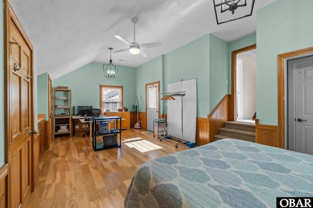 bedroom featuring light wood finished floors, vaulted ceiling, a textured ceiling, and wainscoting