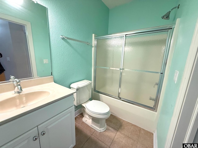 bathroom with a textured wall, tile patterned flooring, toilet, bath / shower combo with glass door, and vanity