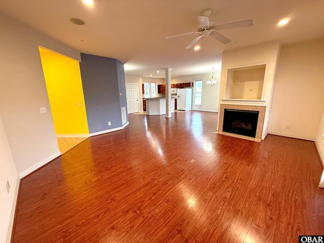 unfurnished living room with baseboards, ceiling fan, wood finished floors, ornate columns, and a fireplace