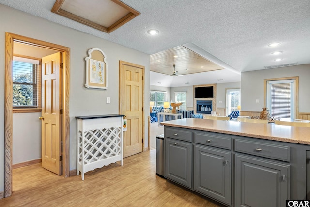 kitchen featuring light wood-type flooring, a glass covered fireplace, gray cabinets, and a textured ceiling