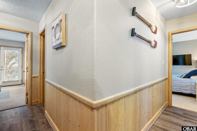 hall featuring a textured ceiling, dark wood-type flooring, and wainscoting