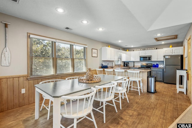 dining area featuring visible vents, a wainscoted wall, light wood-style flooring, a textured ceiling, and wood walls