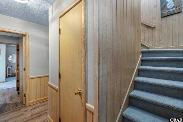 staircase featuring wooden walls, a textured ceiling, wood finished floors, and wainscoting