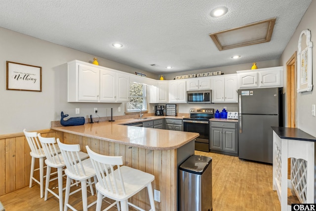 kitchen with a peninsula, stainless steel appliances, gray cabinetry, light wood-style floors, and a sink