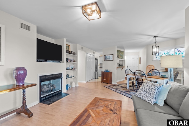 living room featuring built in shelves, baseboards, a fireplace, light wood-style floors, and a notable chandelier