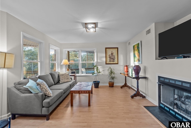 living area with visible vents, a fireplace with flush hearth, baseboards, and light wood finished floors