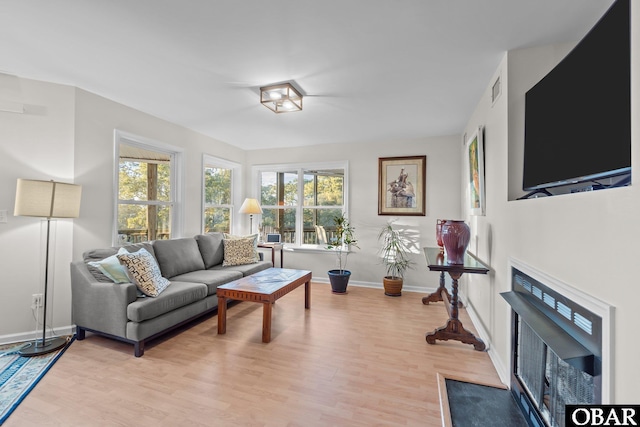 living room featuring baseboards, a fireplace with flush hearth, light wood-style floors, and visible vents