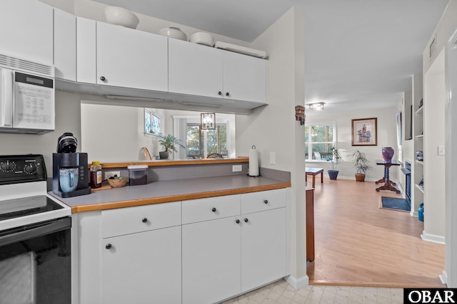 kitchen featuring light countertops, white cabinets, white microwave, and range with electric stovetop