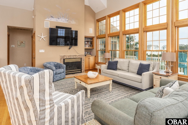 living room with a towering ceiling, light wood finished floors, and a glass covered fireplace