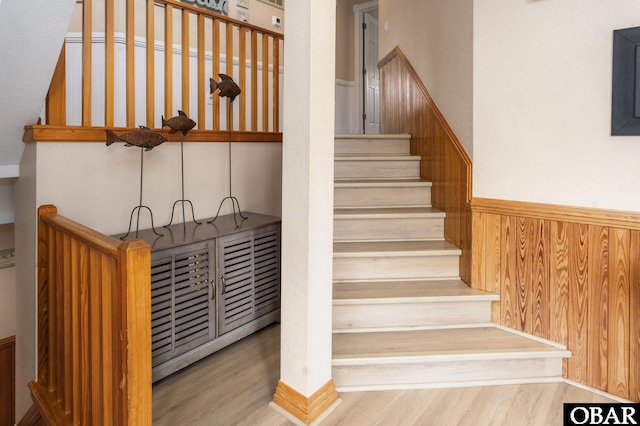 stairway with a wainscoted wall, wooden walls, and wood finished floors