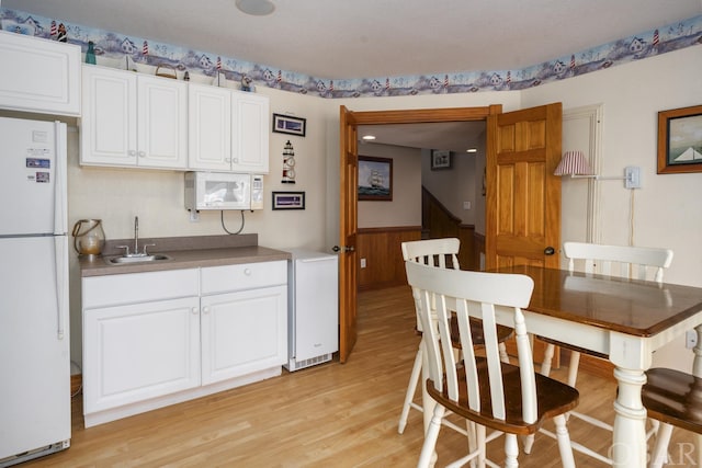 kitchen with light wood finished floors, white appliances, white cabinets, wainscoting, and a sink