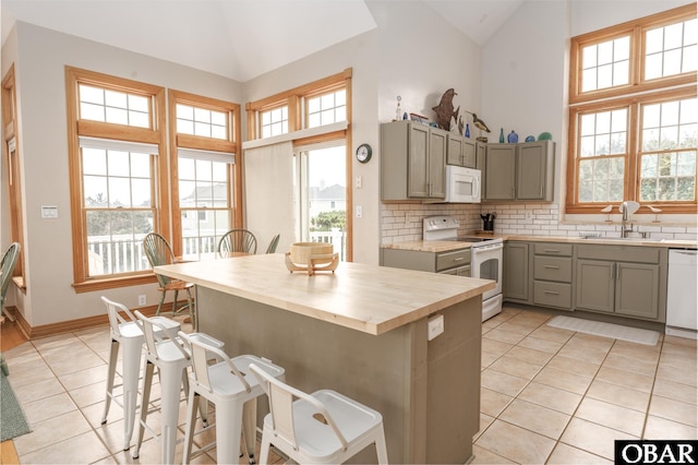 kitchen featuring a breakfast bar, light tile patterned floors, decorative backsplash, a sink, and white appliances