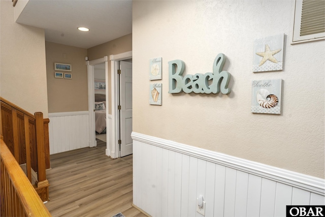 hallway featuring light wood-type flooring, stairs, and wainscoting