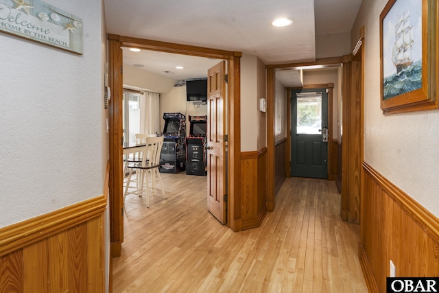 hallway with light wood finished floors, a textured wall, wood walls, and wainscoting