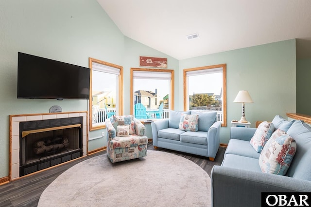 living area with vaulted ceiling, a tiled fireplace, wood finished floors, and visible vents