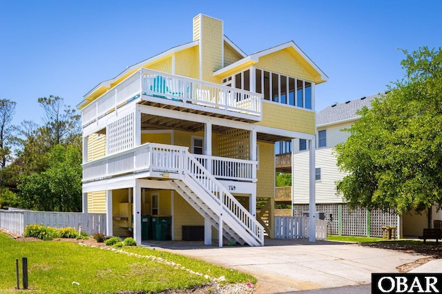 raised beach house featuring driveway, a sunroom, stairway, fence, and a front yard