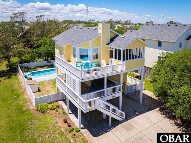 back of house with a fenced in pool, concrete driveway, roof with shingles, and a wooden deck