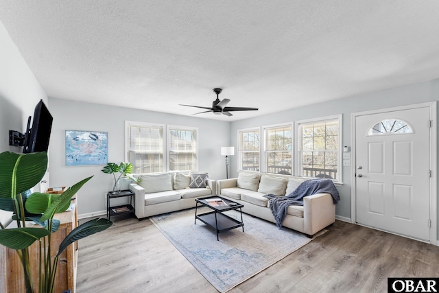 living room featuring a textured ceiling, ceiling fan, light wood-type flooring, and baseboards