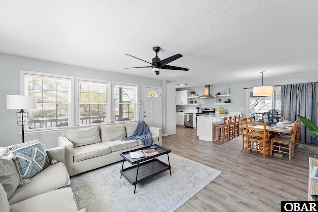 living area featuring a textured ceiling, ceiling fan, and light wood finished floors