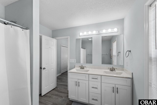 full bath featuring a textured ceiling, double vanity, wood finished floors, and a sink