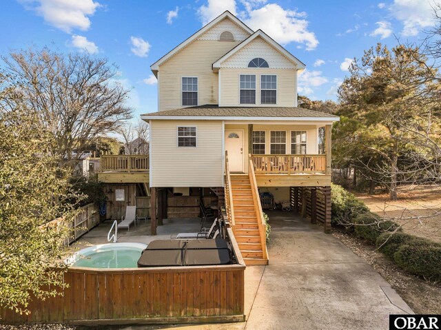 rear view of property featuring a shingled roof, concrete driveway, stairway, fence, and a carport