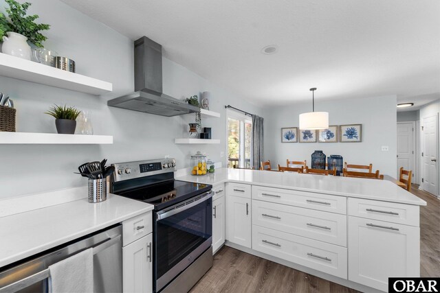 kitchen featuring wall chimney exhaust hood, appliances with stainless steel finishes, hanging light fixtures, a peninsula, and open shelves