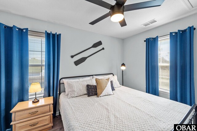 bedroom with a ceiling fan, multiple windows, visible vents, and dark wood-style flooring