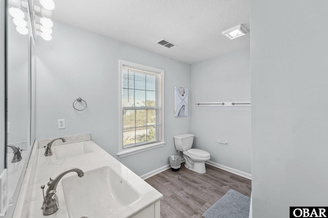 full bath with double vanity, visible vents, a sink, and wood finished floors