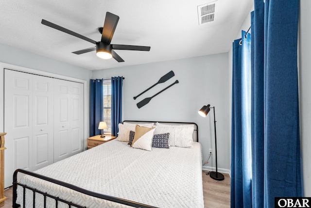 bedroom with ceiling fan, visible vents, baseboards, light wood-style floors, and a closet