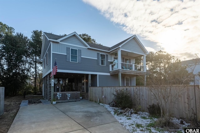 view of front of home with roof with shingles, board and batten siding, fence, a balcony, and driveway