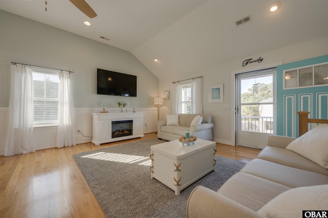 living room with light wood-type flooring, lofted ceiling, wainscoting, and visible vents