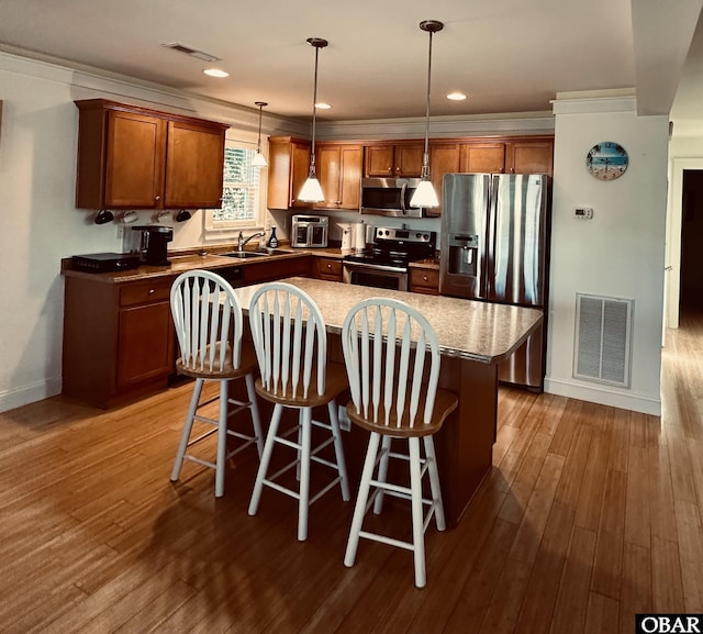 kitchen featuring visible vents, a kitchen island, appliances with stainless steel finishes, decorative light fixtures, and a sink