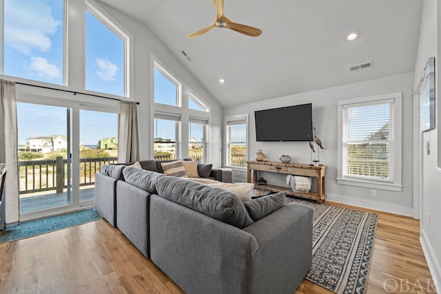 living area with a healthy amount of sunlight, light wood finished floors, visible vents, and high vaulted ceiling