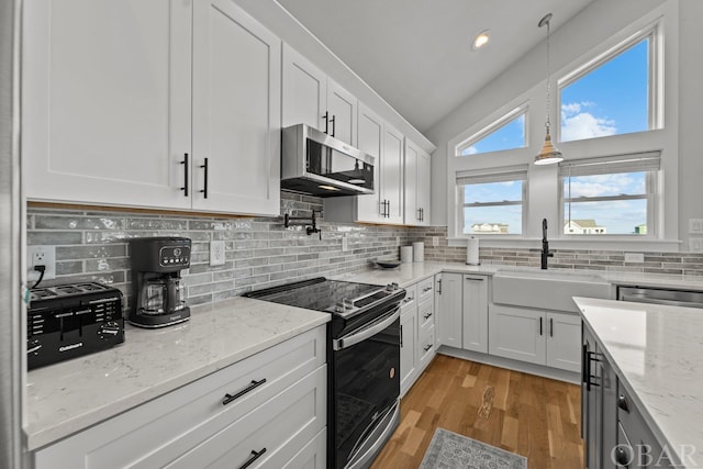 kitchen with decorative light fixtures, light stone countertops, stainless steel appliances, white cabinetry, and a sink