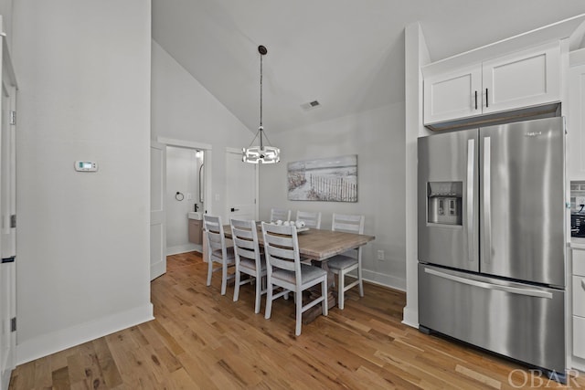 dining area with light wood finished floors, baseboards, visible vents, lofted ceiling, and a chandelier