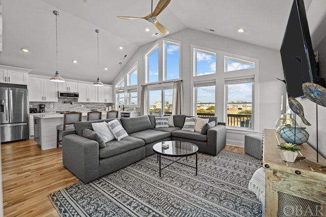 living area with ceiling fan, high vaulted ceiling, light wood-style flooring, and recessed lighting