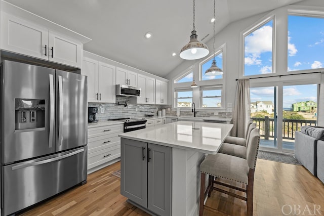 kitchen featuring light stone countertops, stainless steel appliances, a sink, white cabinets, and a center island