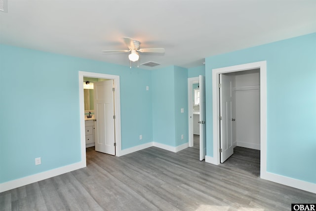 unfurnished bedroom with a walk in closet, visible vents, baseboards, and wood finished floors