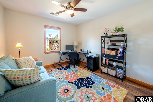 office space featuring a ceiling fan, visible vents, baseboards, and wood finished floors