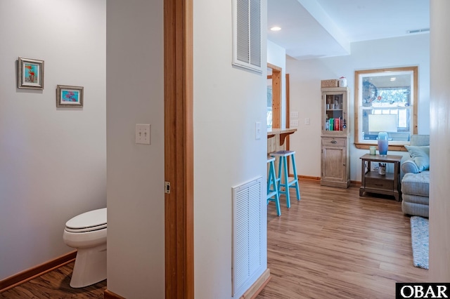 corridor featuring wood finished floors, visible vents, and baseboards