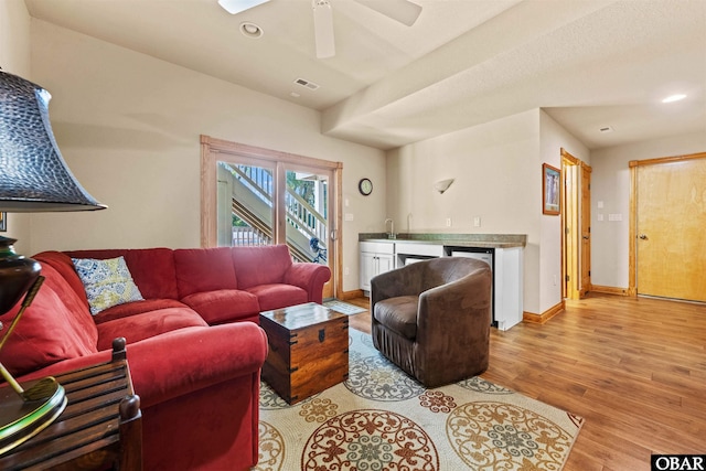 living room with visible vents, baseboards, indoor wet bar, light wood-style flooring, and recessed lighting