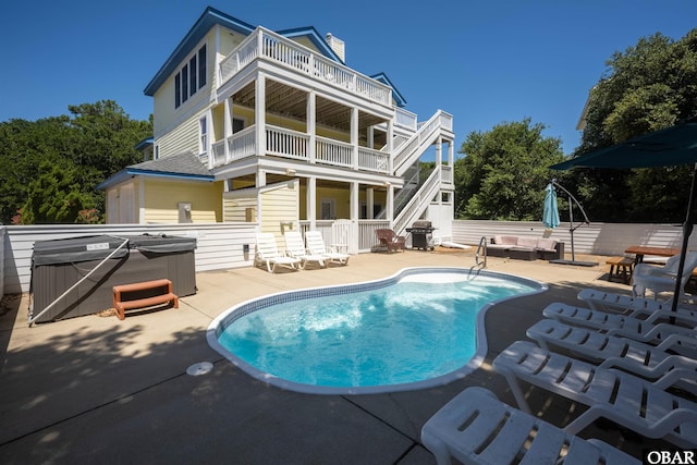 back of property featuring a balcony, a patio area, a fenced in pool, and a hot tub
