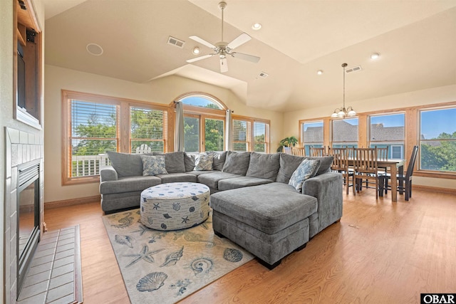 living area with light wood-type flooring, visible vents, a fireplace, and vaulted ceiling