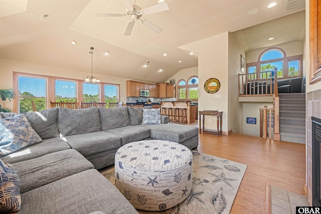 living area with wood finished floors, visible vents, a fireplace with flush hearth, vaulted ceiling, and ceiling fan with notable chandelier