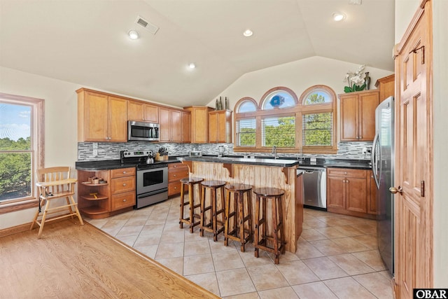 kitchen featuring dark countertops, visible vents, a kitchen bar, vaulted ceiling, and stainless steel appliances