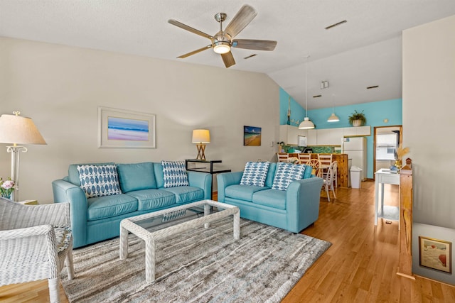 living area featuring lofted ceiling, light wood-style floors, a textured ceiling, and a ceiling fan