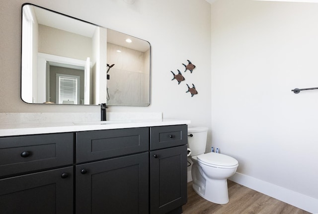 bathroom featuring toilet, wood finished floors, vanity, baseboards, and walk in shower