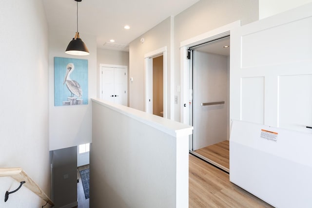 corridor with light wood finished floors, an upstairs landing, and recessed lighting