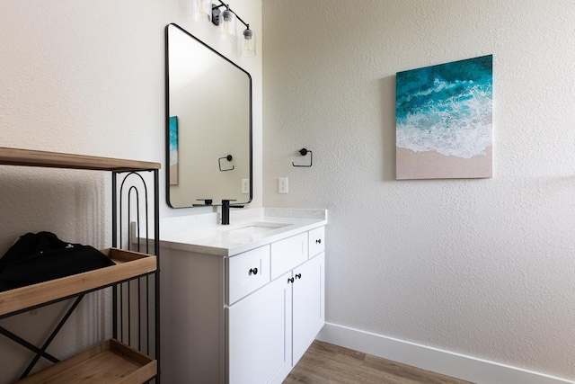 bathroom featuring vanity, baseboards, wood finished floors, and a textured wall