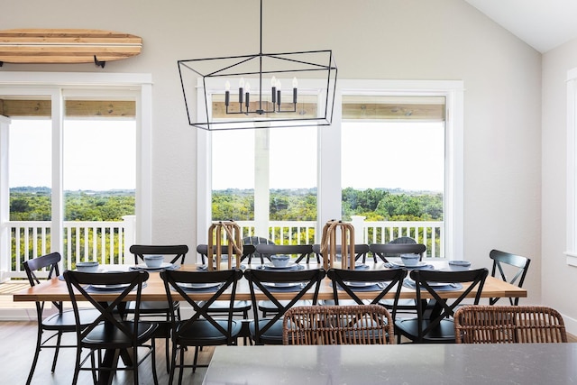 dining room featuring a healthy amount of sunlight, a chandelier, vaulted ceiling, and wood finished floors